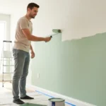 A man confidently painting a living room wall light green with a roller, demonstrating how to paint walls like a pro in a DIY home improvement project.