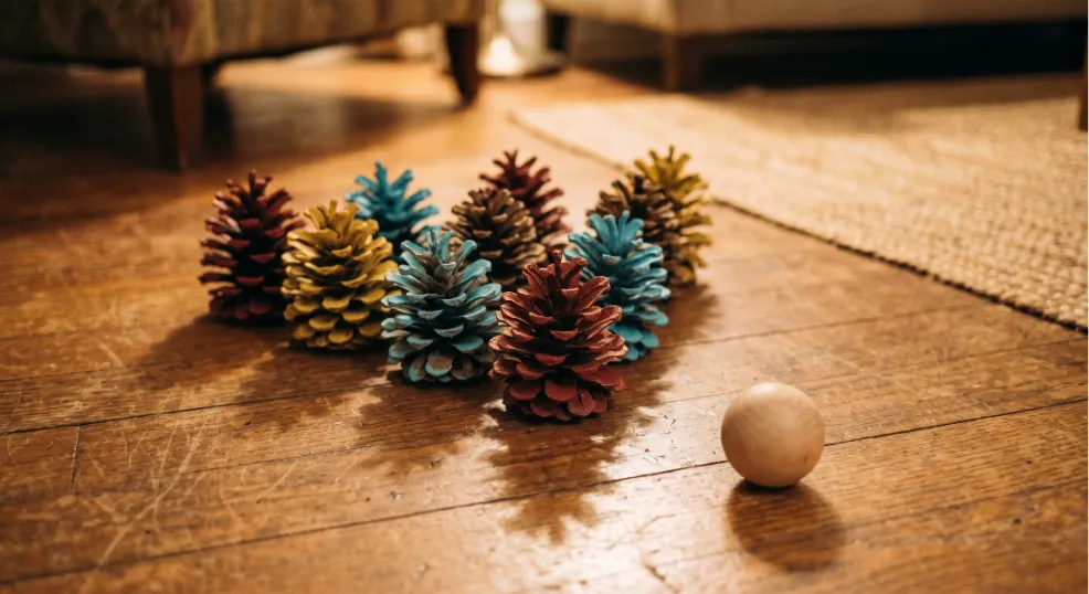 Painted pine cones arranged as bowling pins on a hardwood floor for an indoor kids game.