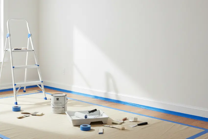 A clean, white wall prepped and ready for painting with painter's tape and drop cloths, showing the final step after old wallpaper has been removed.