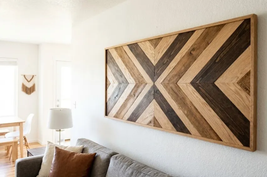 A large DIY geometric wood wall art piece featuring a chevron pattern made from contrasting natural and dark stained scrap wood slats.