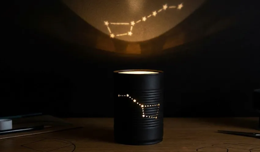 A DIY constellation night light made from a black-painted tin can with holes punched in the shape of the Big Dipper, projecting the star pattern onto a dark wall.