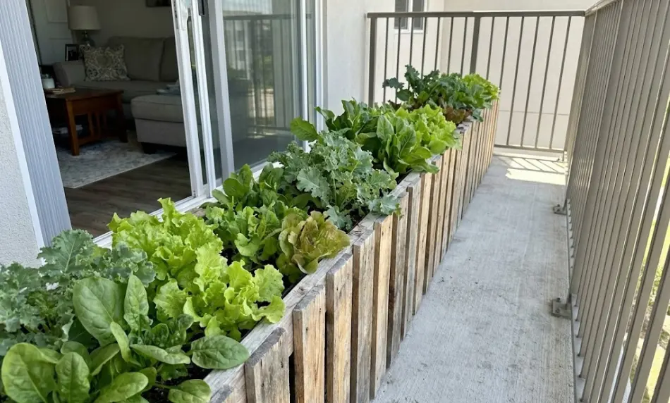 A slim, rectangular wooden pallet planter (approximately 18 inches wide) positioned along a metal balcony railing; it is filled with marigolds and basil, leaving ample walking space on the tiled floor.