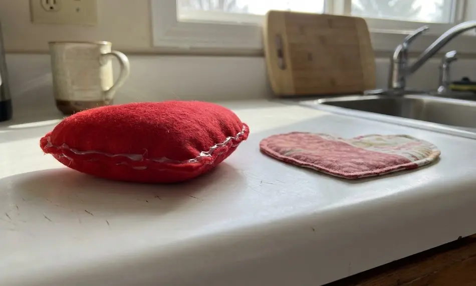 Side-by-side comparison on a white counter: a puffy, stuffed red felt heart with visible glue seams (left) versus a flat, patterned fabric heart (right).