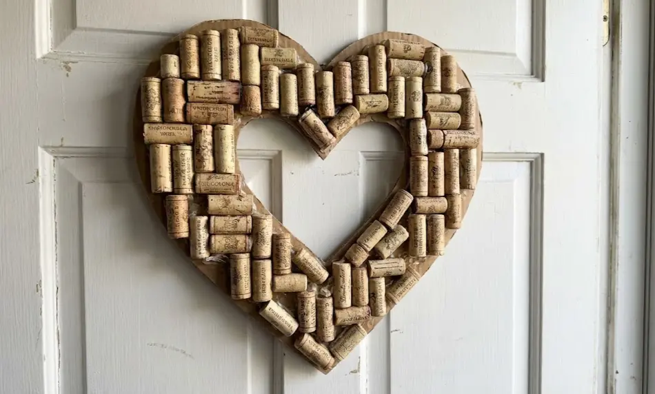 Front view of a rustic heart-shaped wreath crafted from used wine corks glued onto a cardboard backing, hanging on a white interior door.