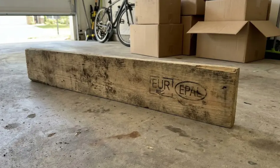 close-up of a single, rough-sawn wooden pallet plank lying on a concrete garage floor, featuring a prominent black "EUR EPAL" shipping logo stamped on the side.