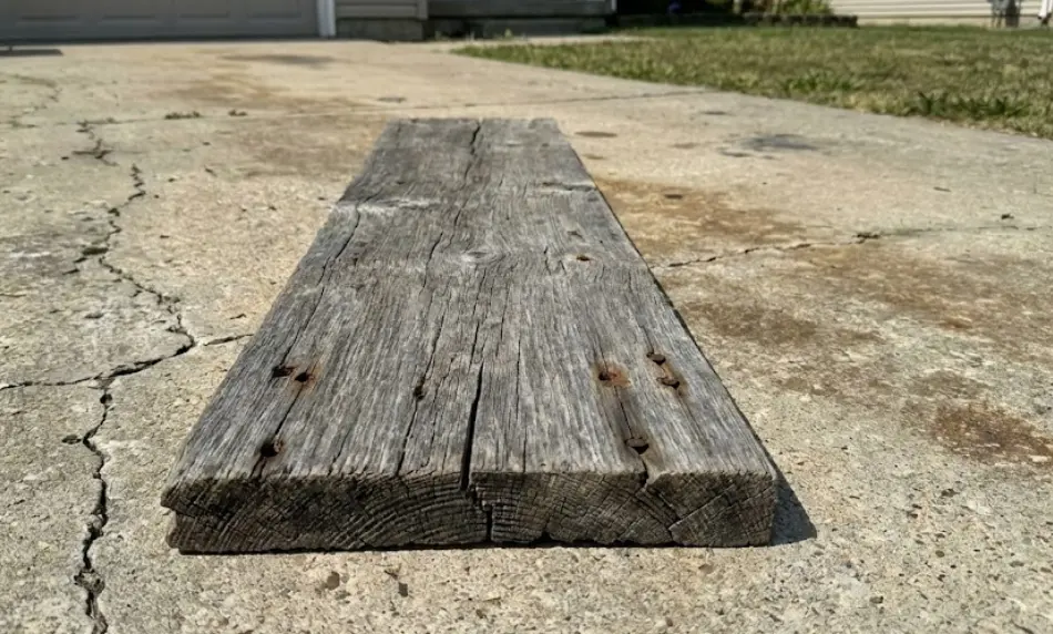 close-up detail shot of antique reclaimed wood planks showing deep weather-beaten silver patina, distinct black rusted nail holes, and rough circular saw marks across the grain.