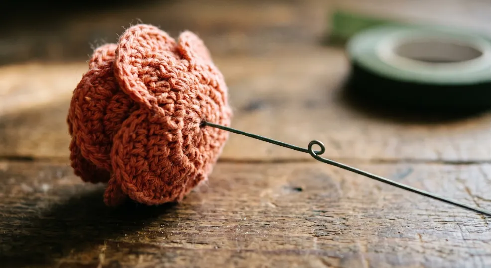 Attaching a floral wire loop to the base of a crocheted rose to create a sturdy stem.